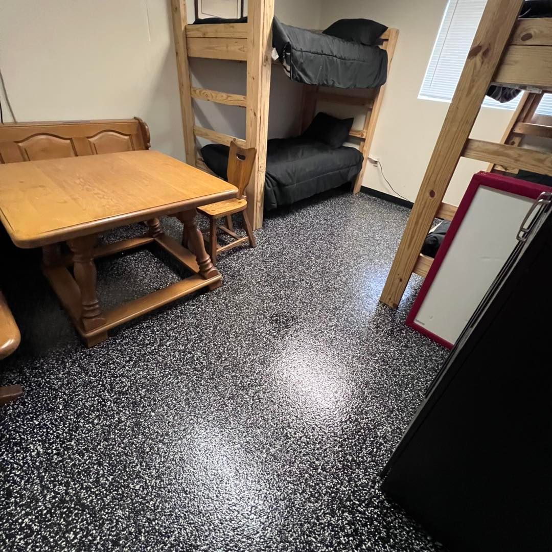 Room with a bunk bed, table, and chairs. The floor is black and gray speckled.