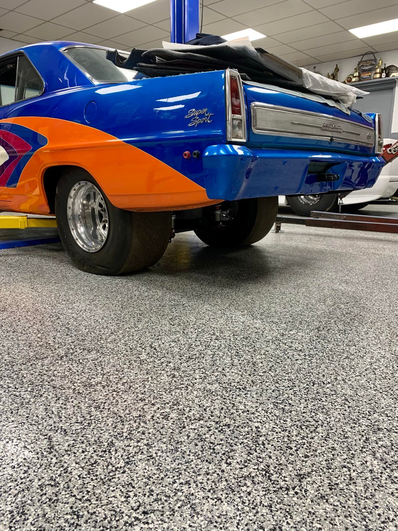 Blue and orange race car on a speckled floor in a garage.