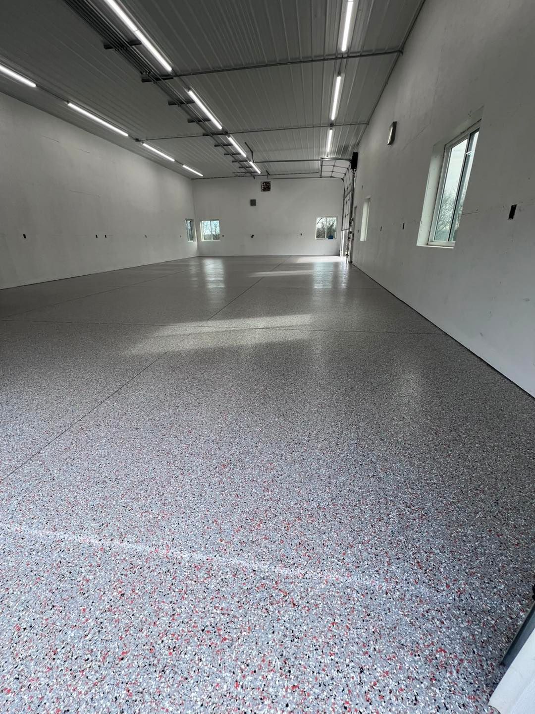 A large, empty industrial space with a speckled floor and bright overhead lights.