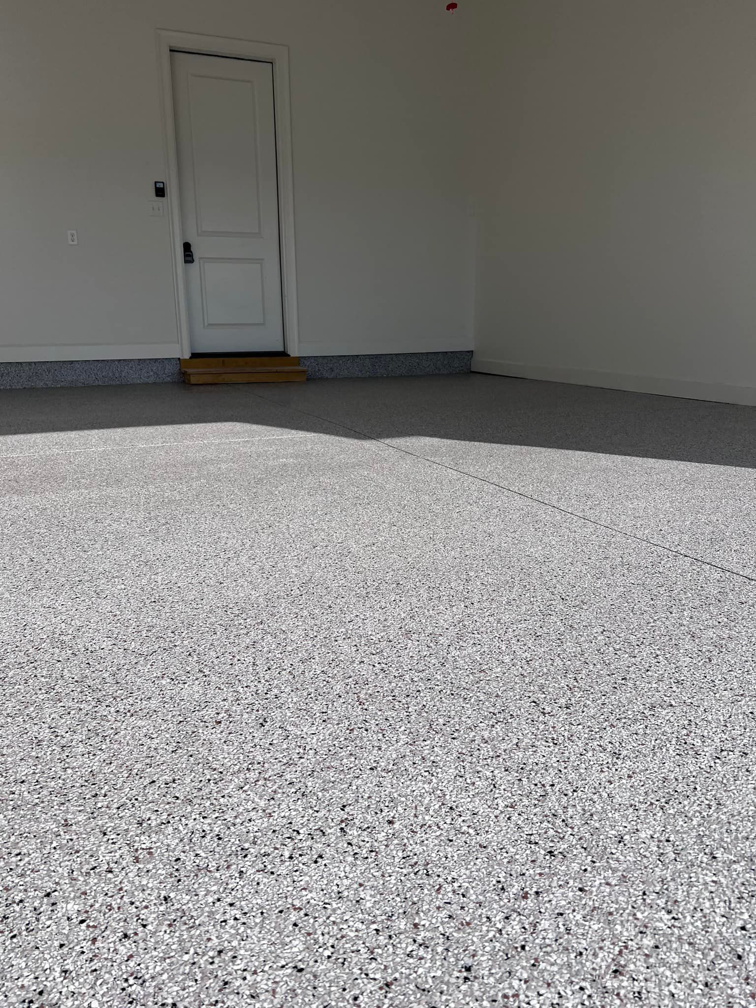 Garage with speckled gray and white floor, white walls, and a white door with a step.