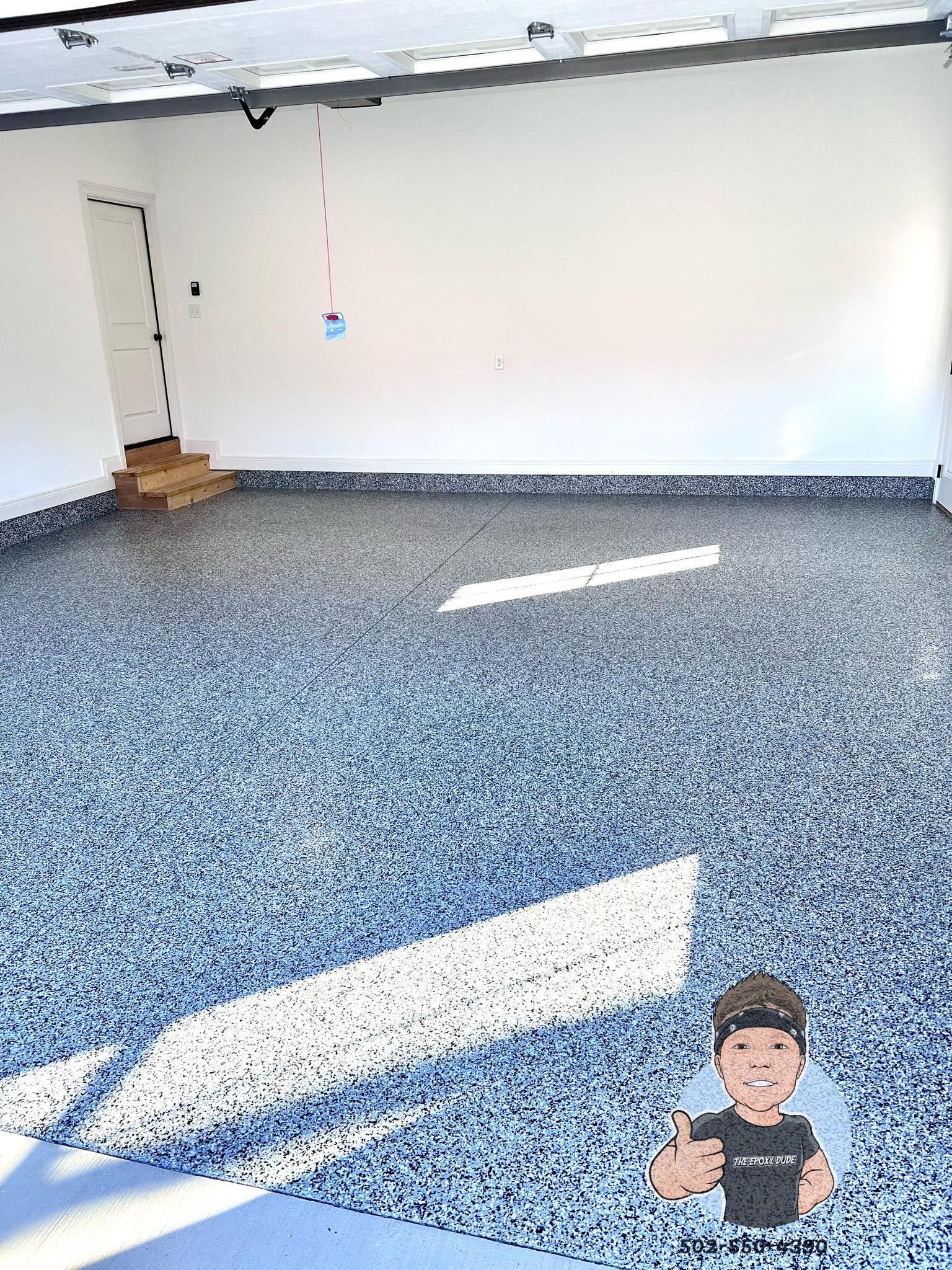 Garage with speckled epoxy floor, white walls, and a doorway. Sunlight streams across the floor.