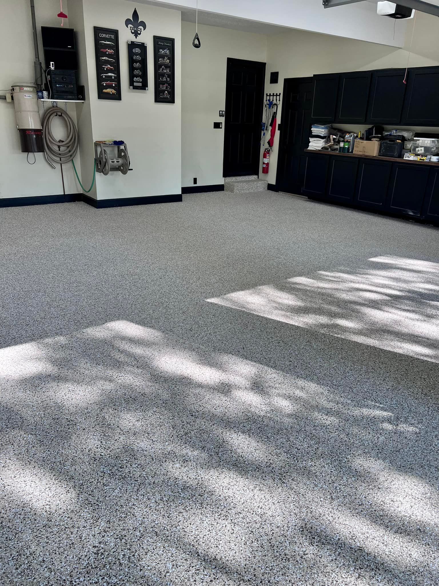 Garage with speckled flooring, cabinets, and various wall-mounted items.