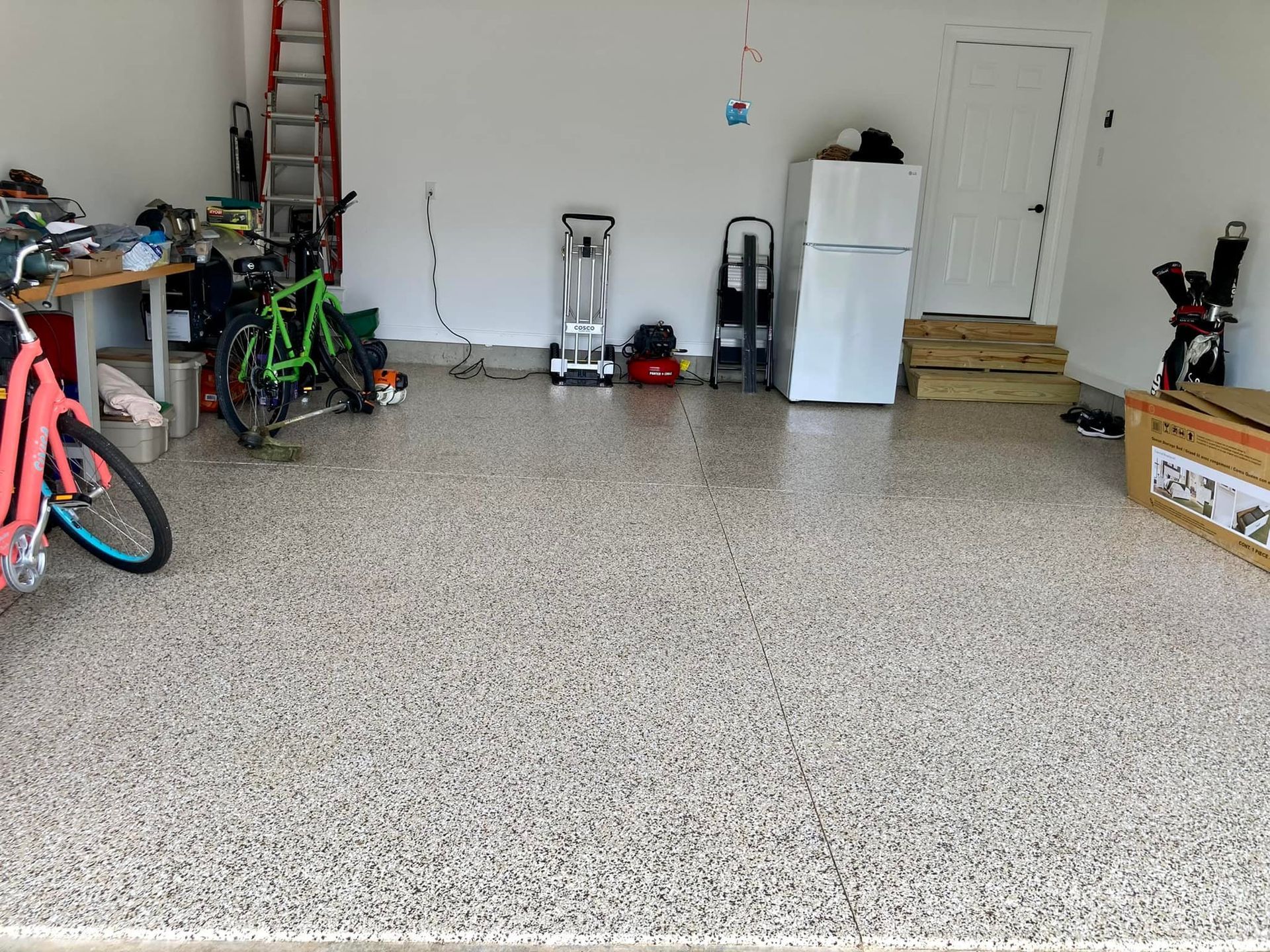 Garage interior with epoxy flooring, cluttered with bikes, tools, and a refrigerator.