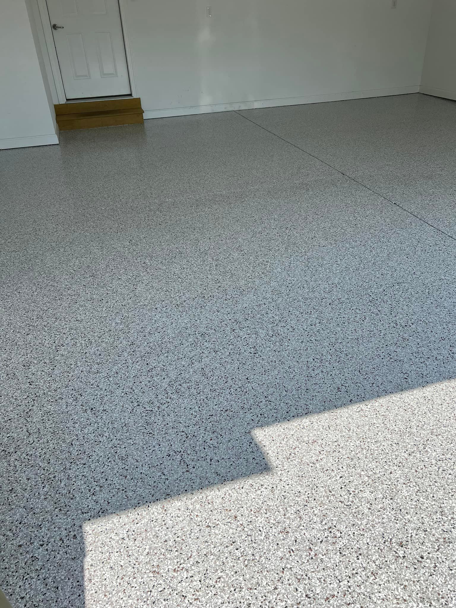Epoxy garage floor speckled with white, gray, and black chips. Door visible at back.