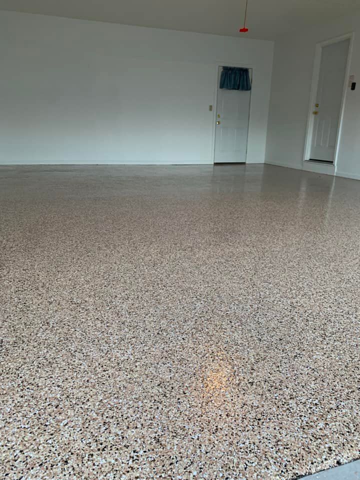 Polished concrete garage floor with speckled brown, beige, and gray aggregate. White walls, a door, and overhead lighting.