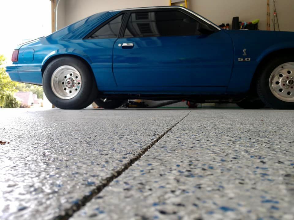 Blue Mustang car parked in a garage with a speckled floor.