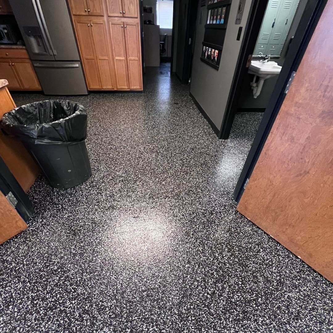 Black and white speckled flooring in a kitchen area with cabinets, appliances, and a hallway to a bathroom.