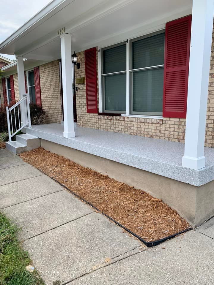A house with a porch. Red shutters, gray speckled porch floor, and mulch bed along the sidewalk.