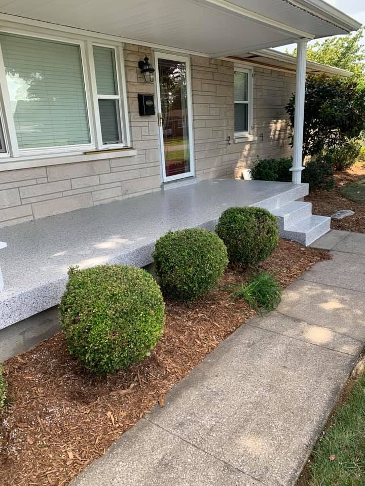 Front of a house with light stone exterior, a concrete porch, and manicured shrubs.