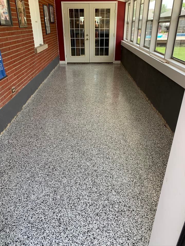 Epoxy-coated floor in a sunroom with white doors and brick wall. Speckled gray and white floor, natural light.