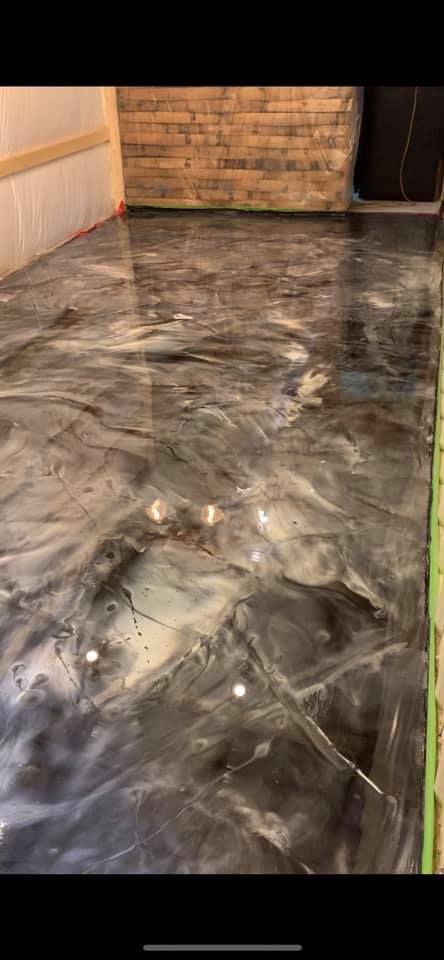 Metallic epoxy flooring with swirling black, gray, and white patterns, a brick wall, and a wooden trim.