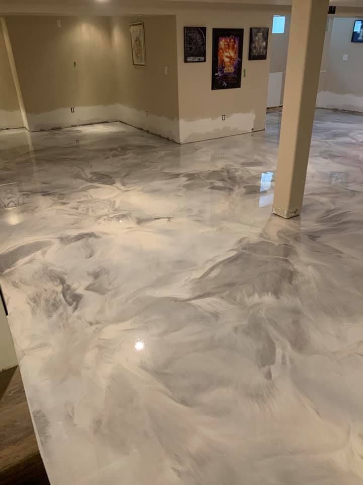 Epoxy-coated floor in shades of white and gray, reflecting light. Bare walls and a support beam are visible.