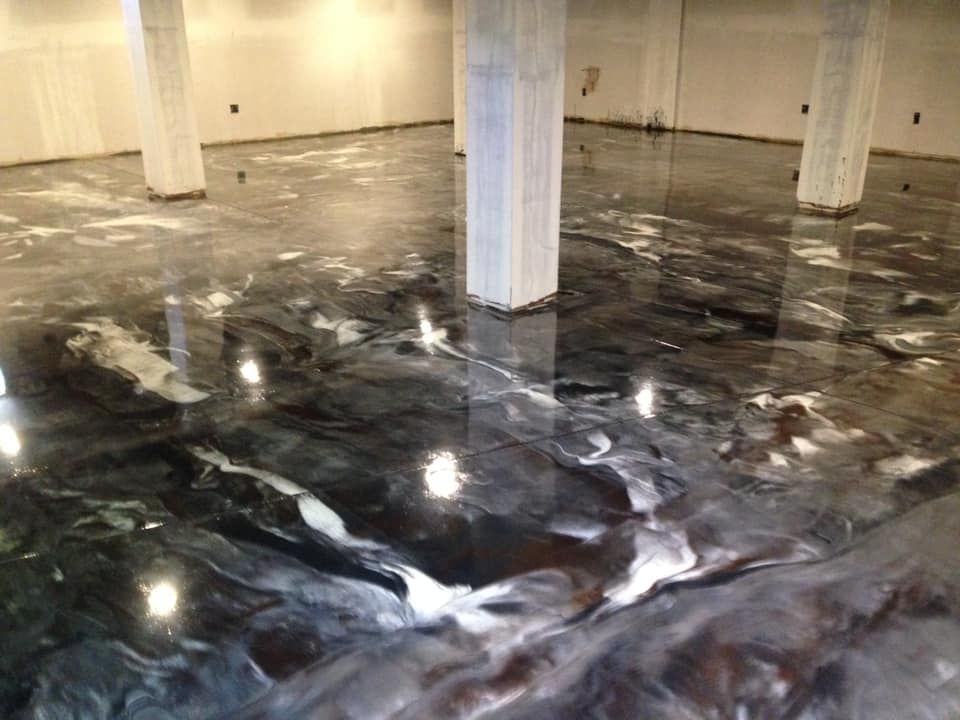 Glossy epoxy floor with dark, swirling patterns, concrete pillars, bright reflections.