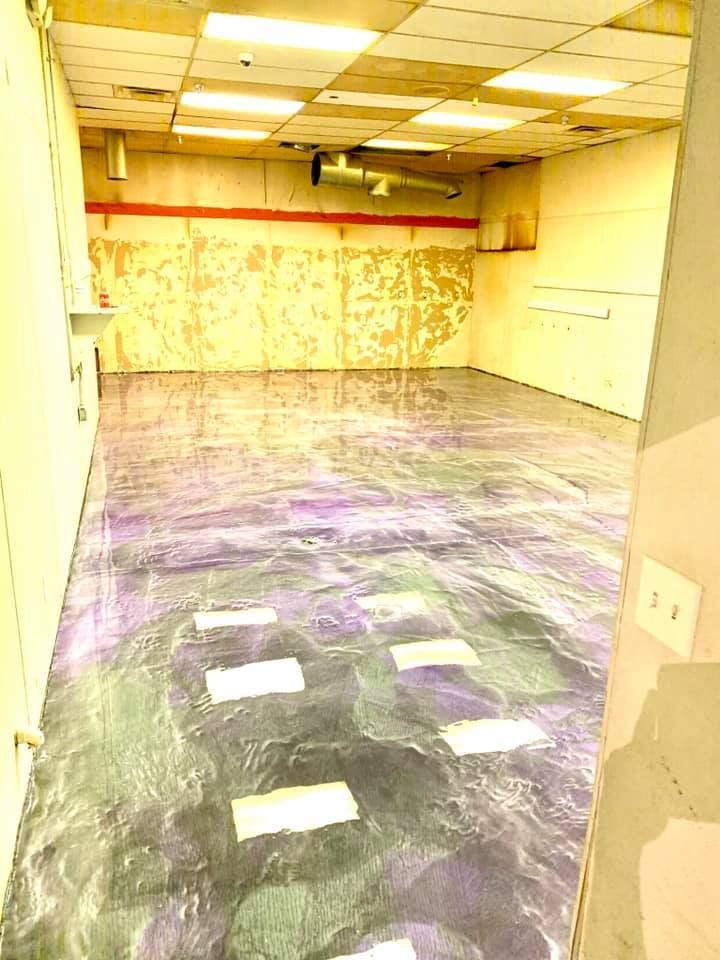 Empty room with shiny, patterned floor. Walls are beige, with peeling paint. Fluorescent ceiling lights.