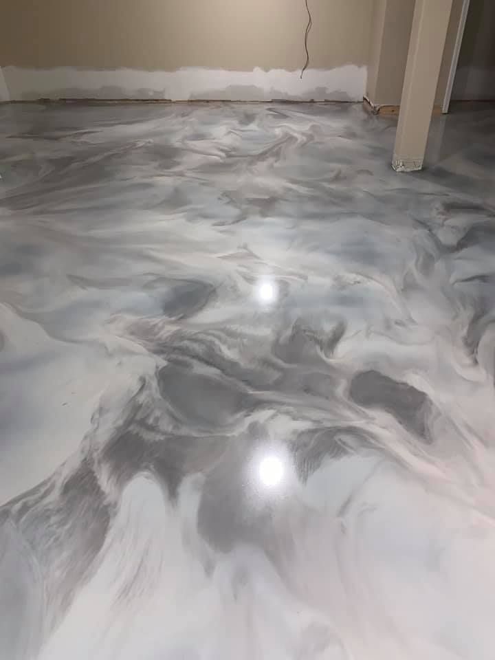 Metallic silver and white epoxy floor with swirling patterns in a room, concrete walls.