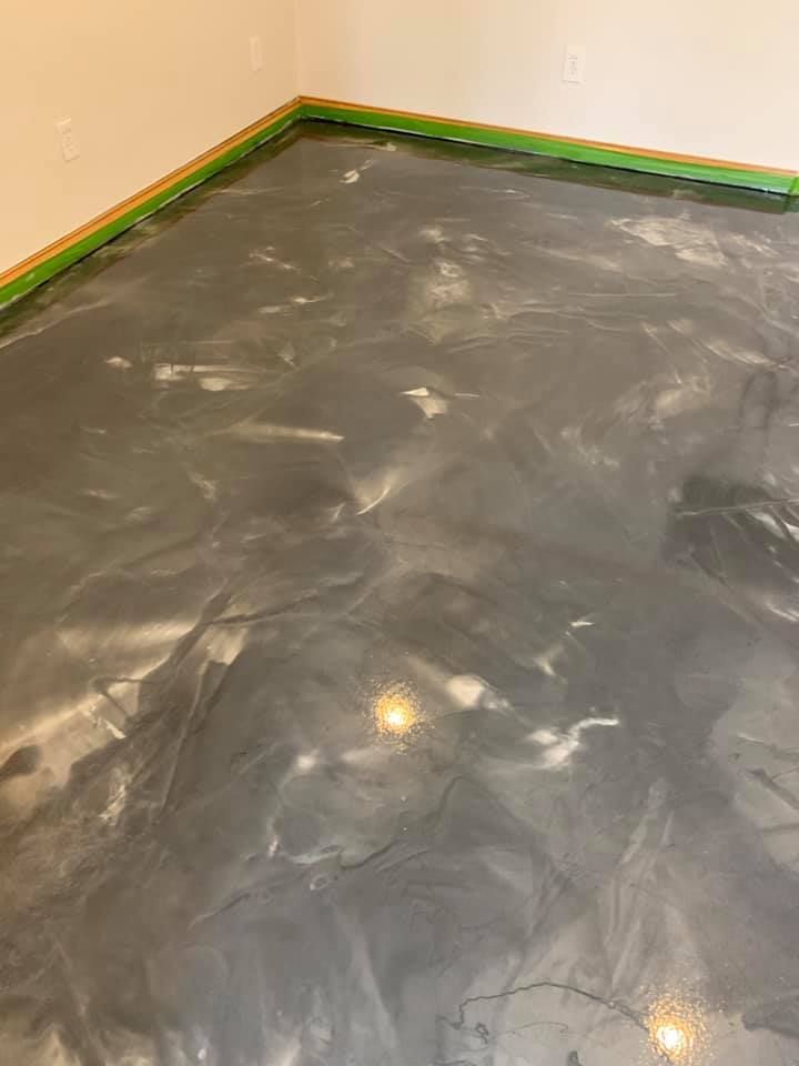 Gray epoxy floor with marbled, swirling effect, green tape along the wall.