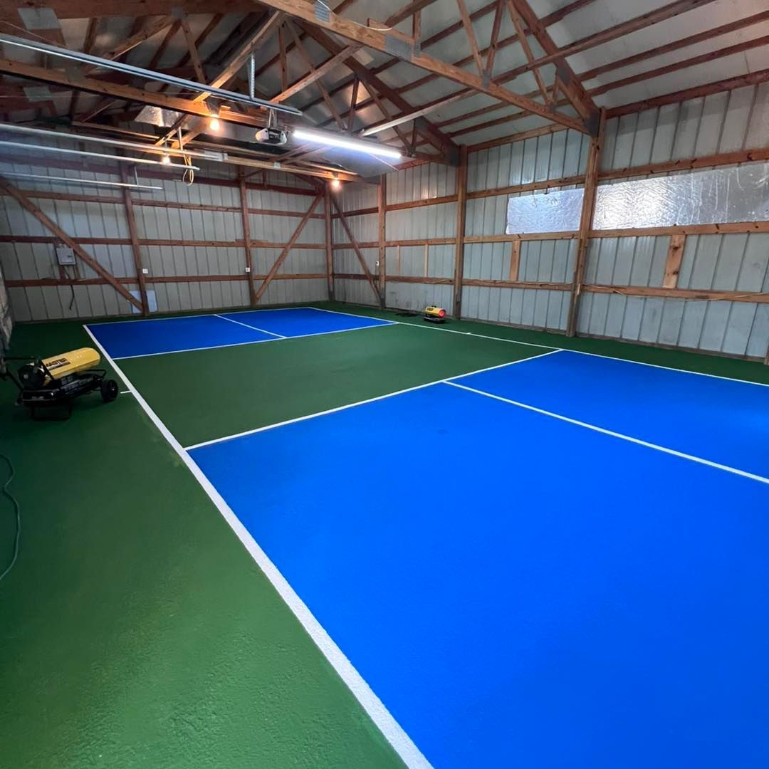 Indoor pickleball court with blue and green playing surfaces, white lines, and wood framing.
