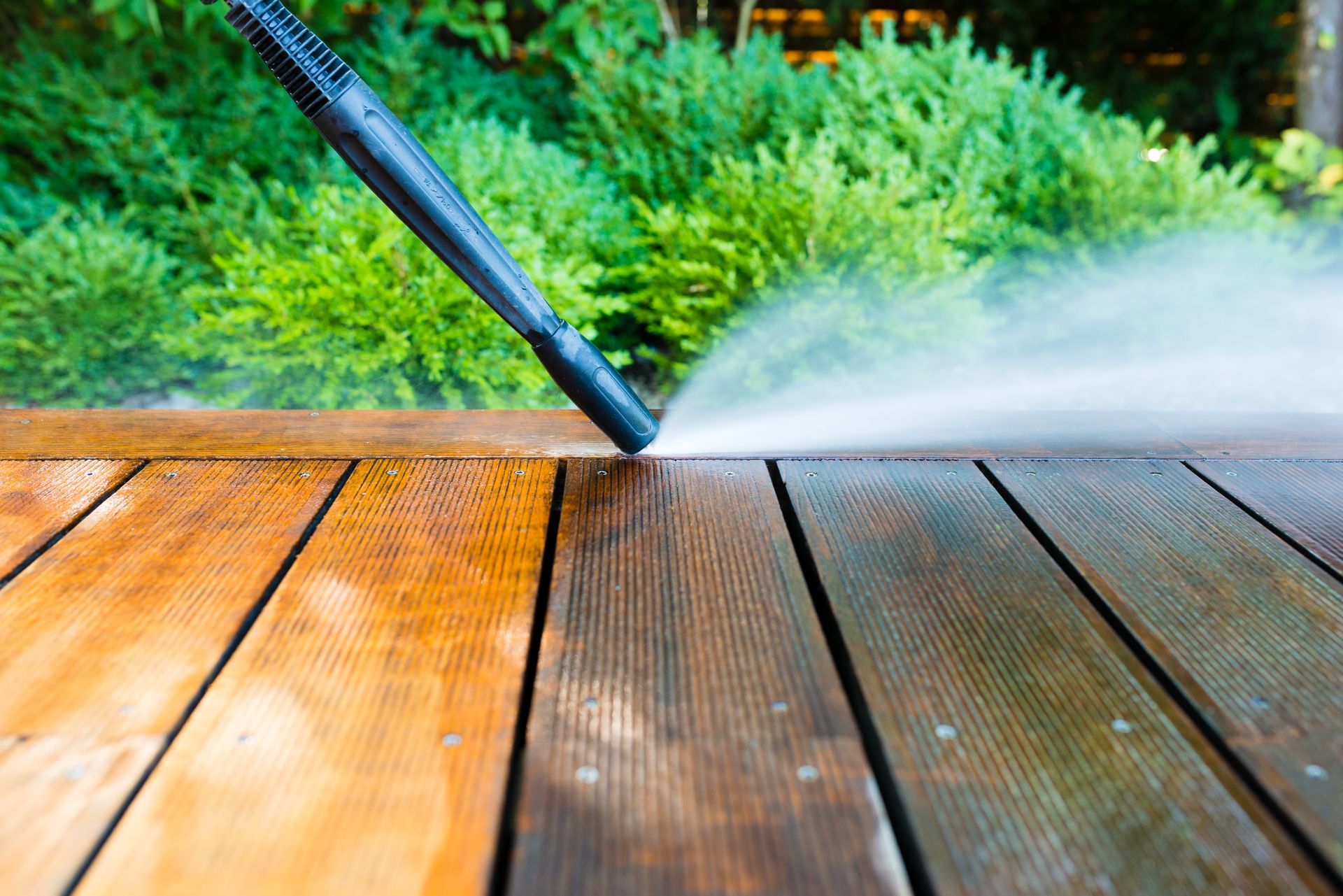 A person is using a high pressure washer to clean a wooden deck.