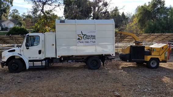 White truck with enclosed bed and yellow wood chipper connected, parked outdoors.