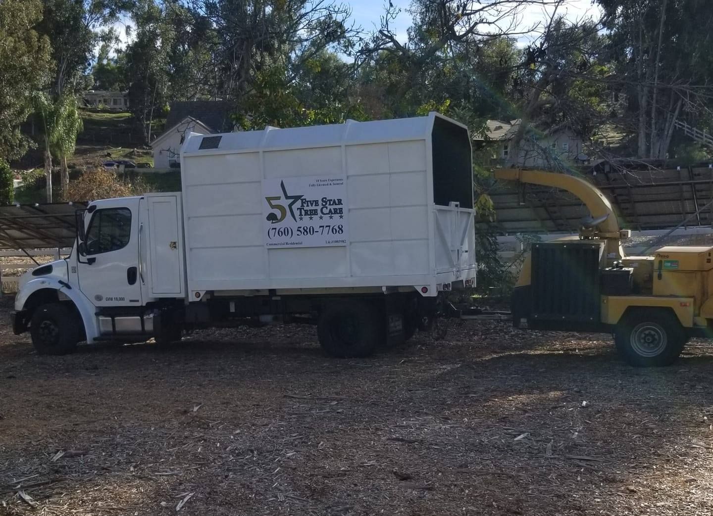 White truck with attached wood chipper; parked on gravel, trees in background.