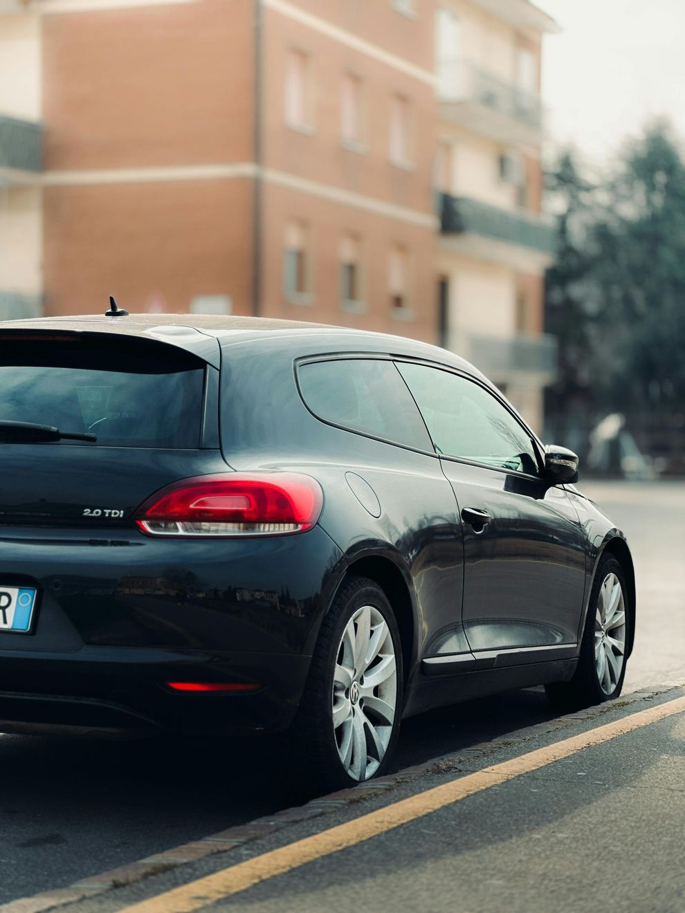 Una berlina nera parcheggiata in strada accanto a un edificio in mattoni, vista da dietro.