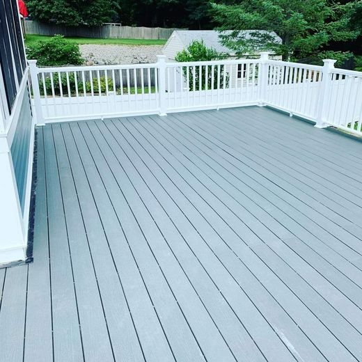 A gray deck with a white railing and trees in the background