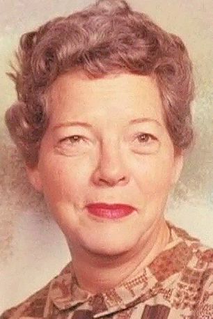 Woman with curly gray hair and red lipstick, wearing a patterned blouse, smiling.