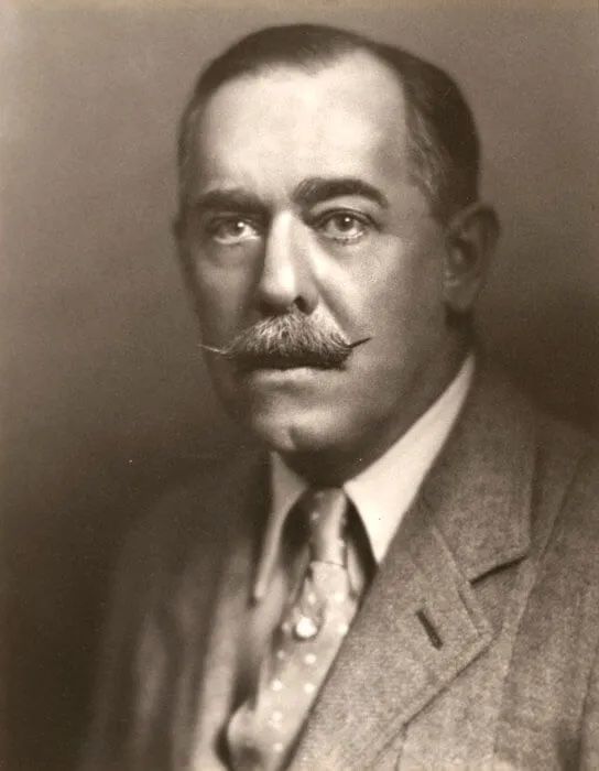 Man in suit with mustache looking at the viewer.