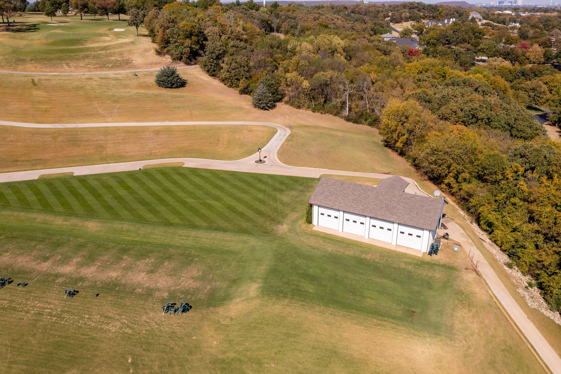 An aerial view of a building with a brown roof on a green lawn, next to a path and a golf course.