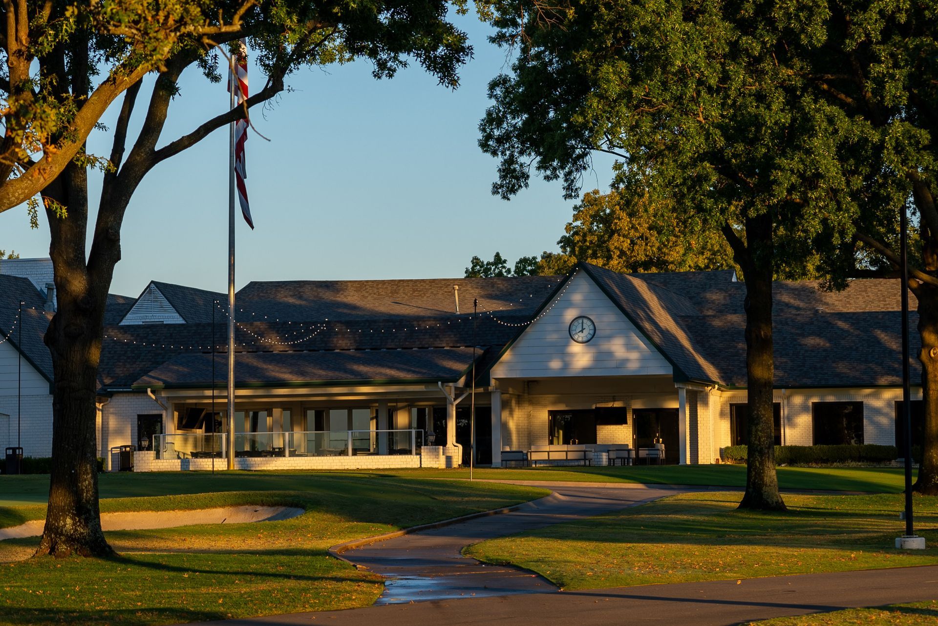 Building with a gray roof and a white facade, flagpole, and trees in a grassy setting.