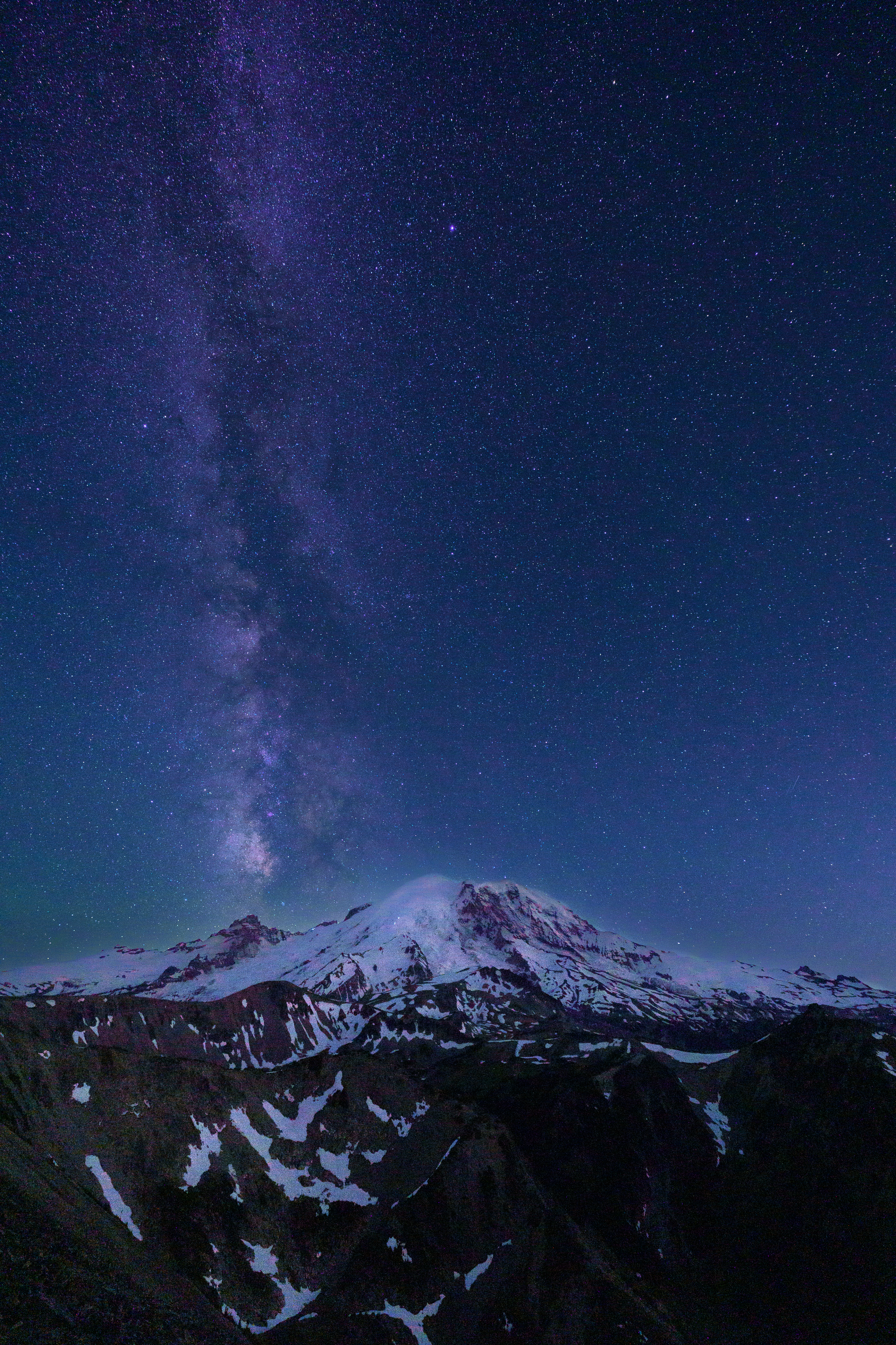 The milky way is visible over a mountain at night.