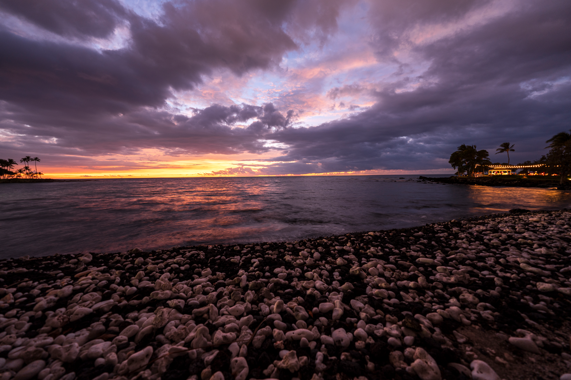 A sunset over a body of water with a lot of rocks on the beach.