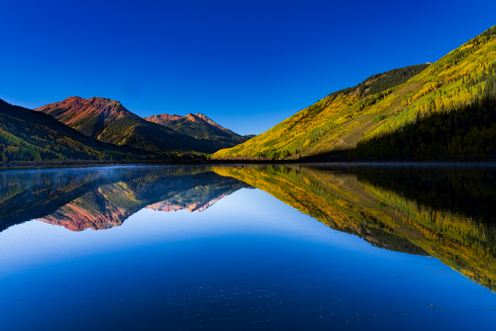 A lake surrounded by mountains and trees is reflected in the water.