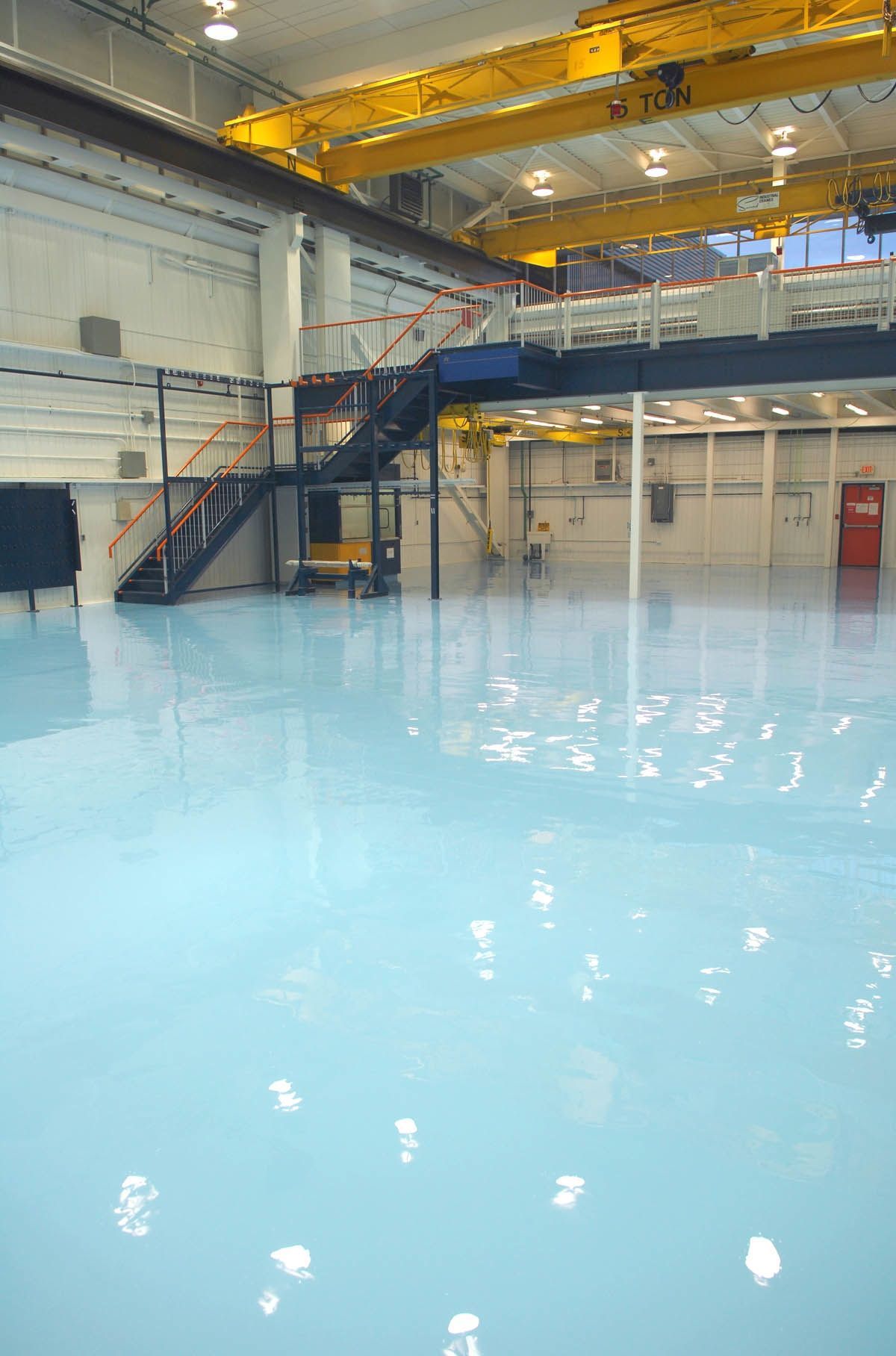 A large empty warehouse with a blue floor and stairs.