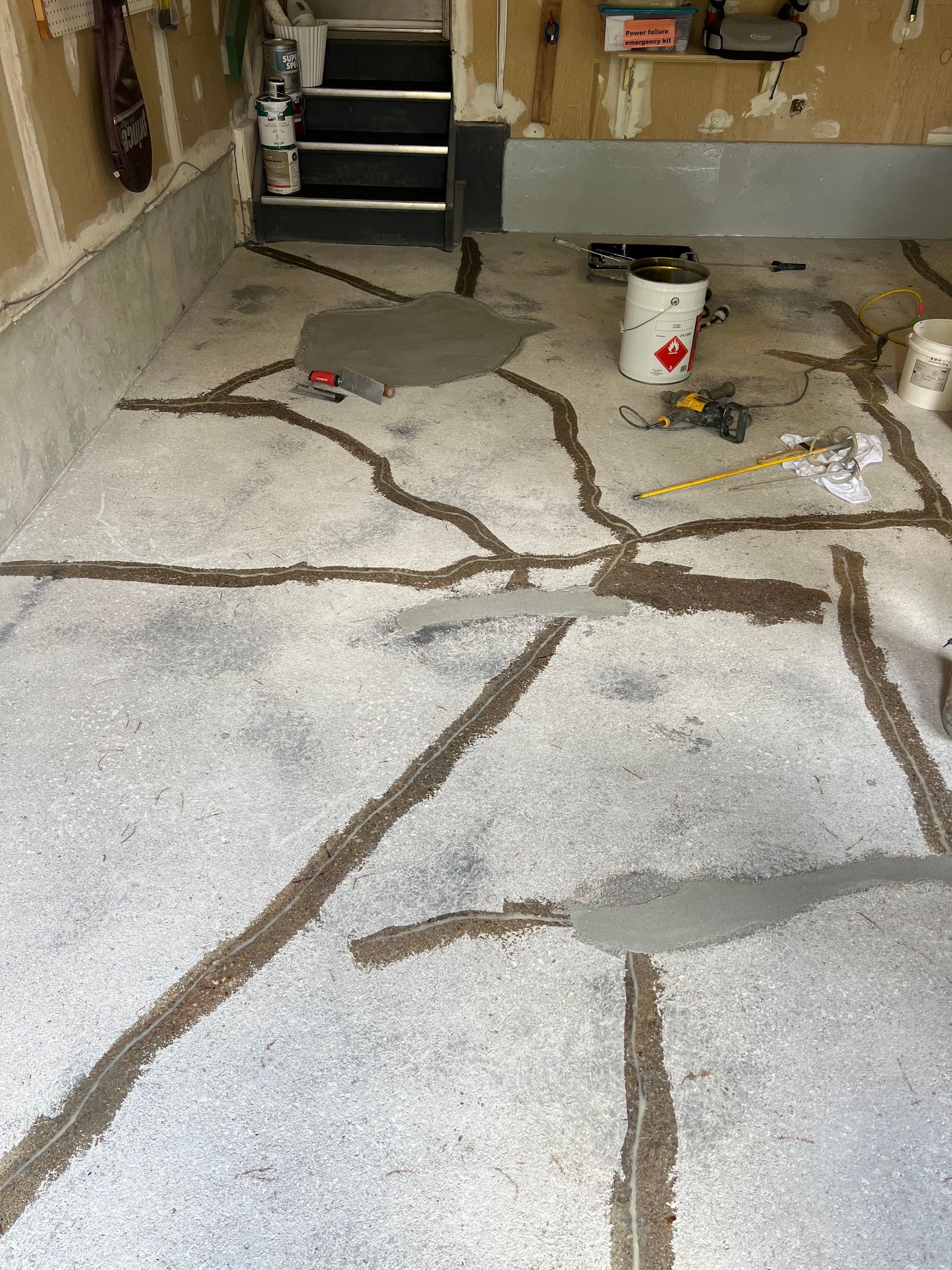 A garage floor with a bucket of paint and a measuring tape on it.