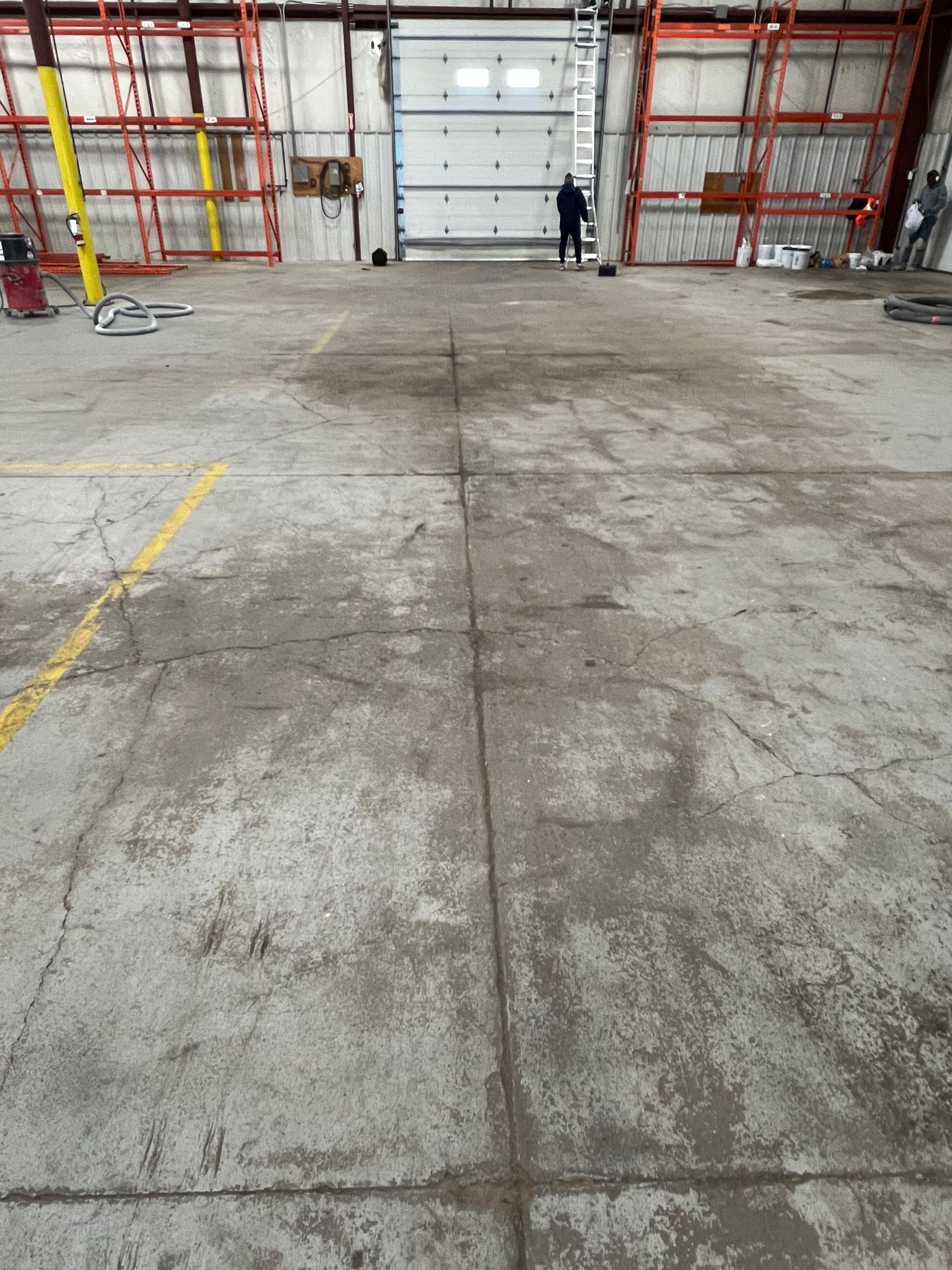 A dirty concrete floor in a warehouse with a ladder in the background