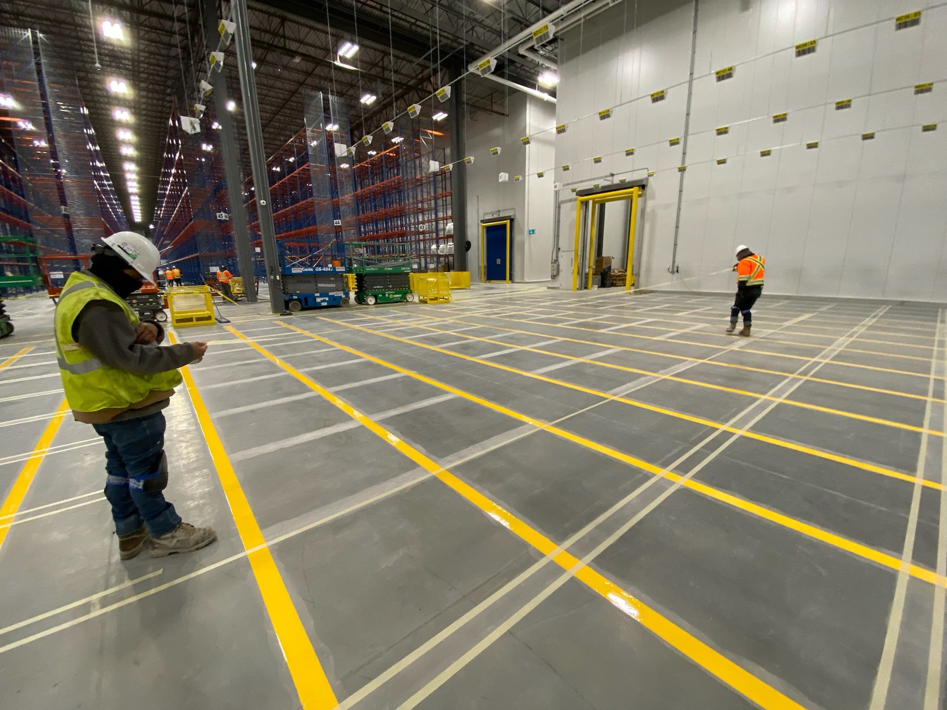 A man is standing in a large warehouse with yellow lines on the floor.