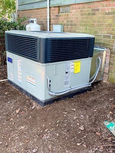 A large air conditioner is sitting in the dirt in front of a brick building.