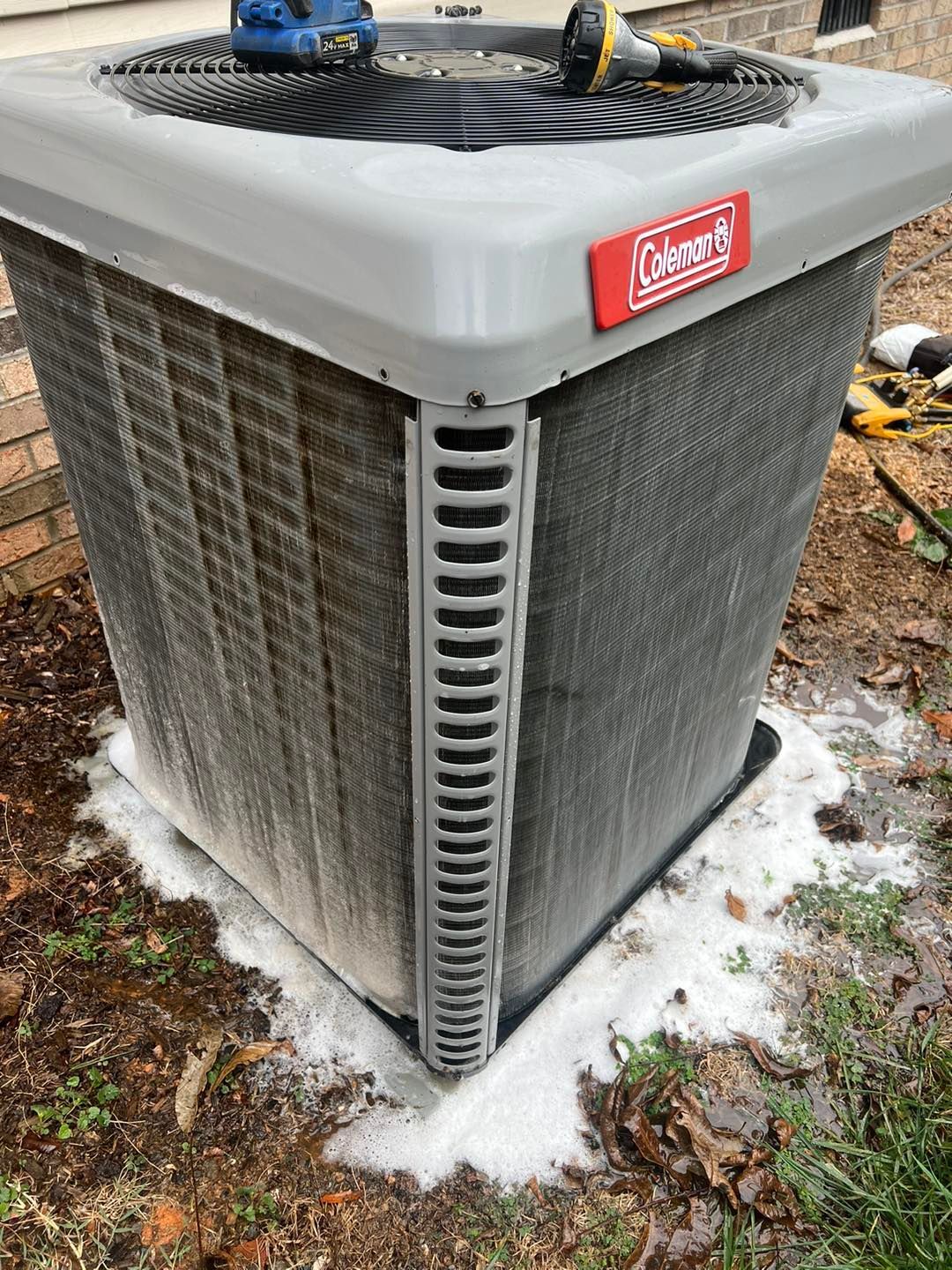 A coleman air conditioner is sitting on the ground next to a house.