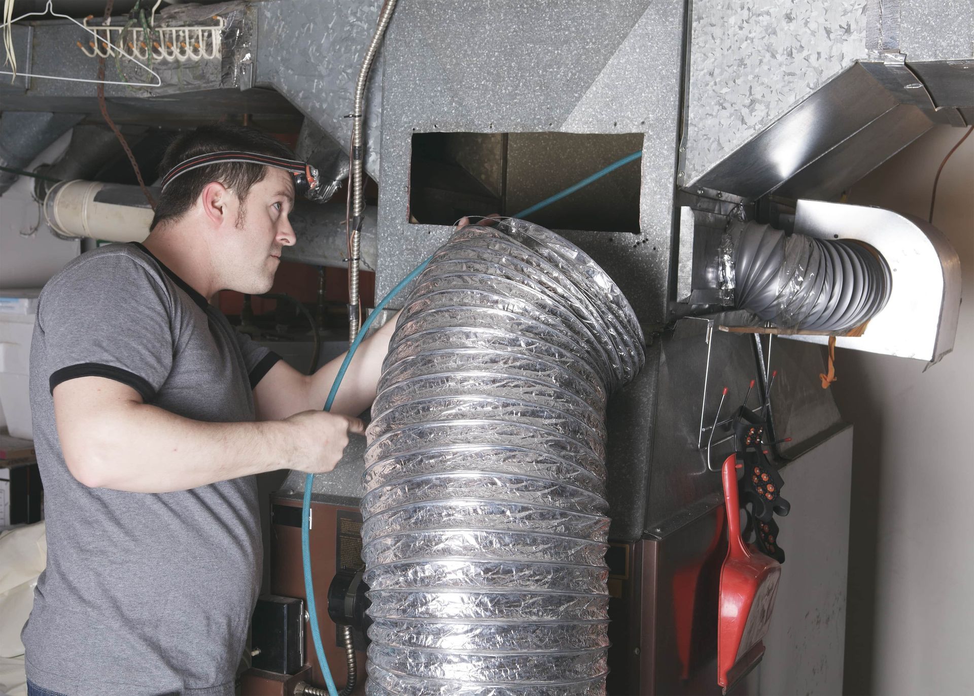 A man is working on a ventilation system in a basement.