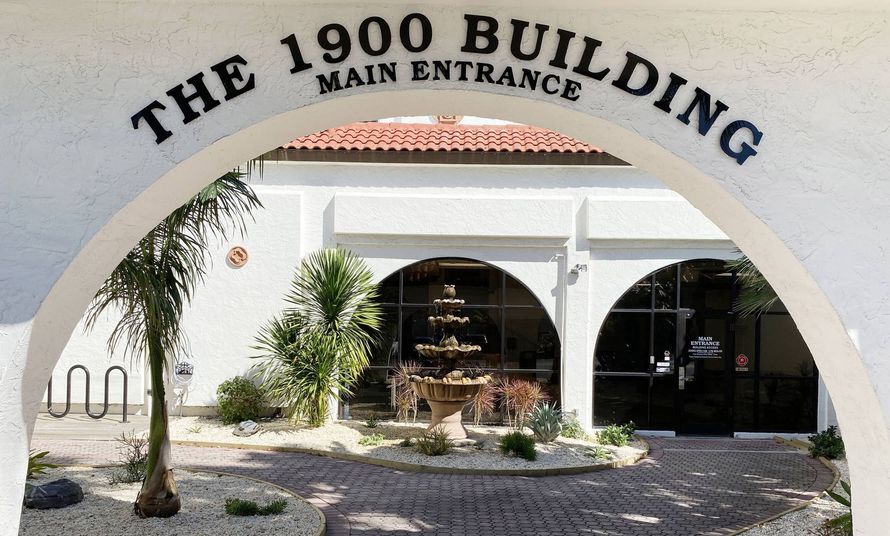 Entrance arch reading “The 1900 Building” over a white stucco entry with plants and outdoor seating.