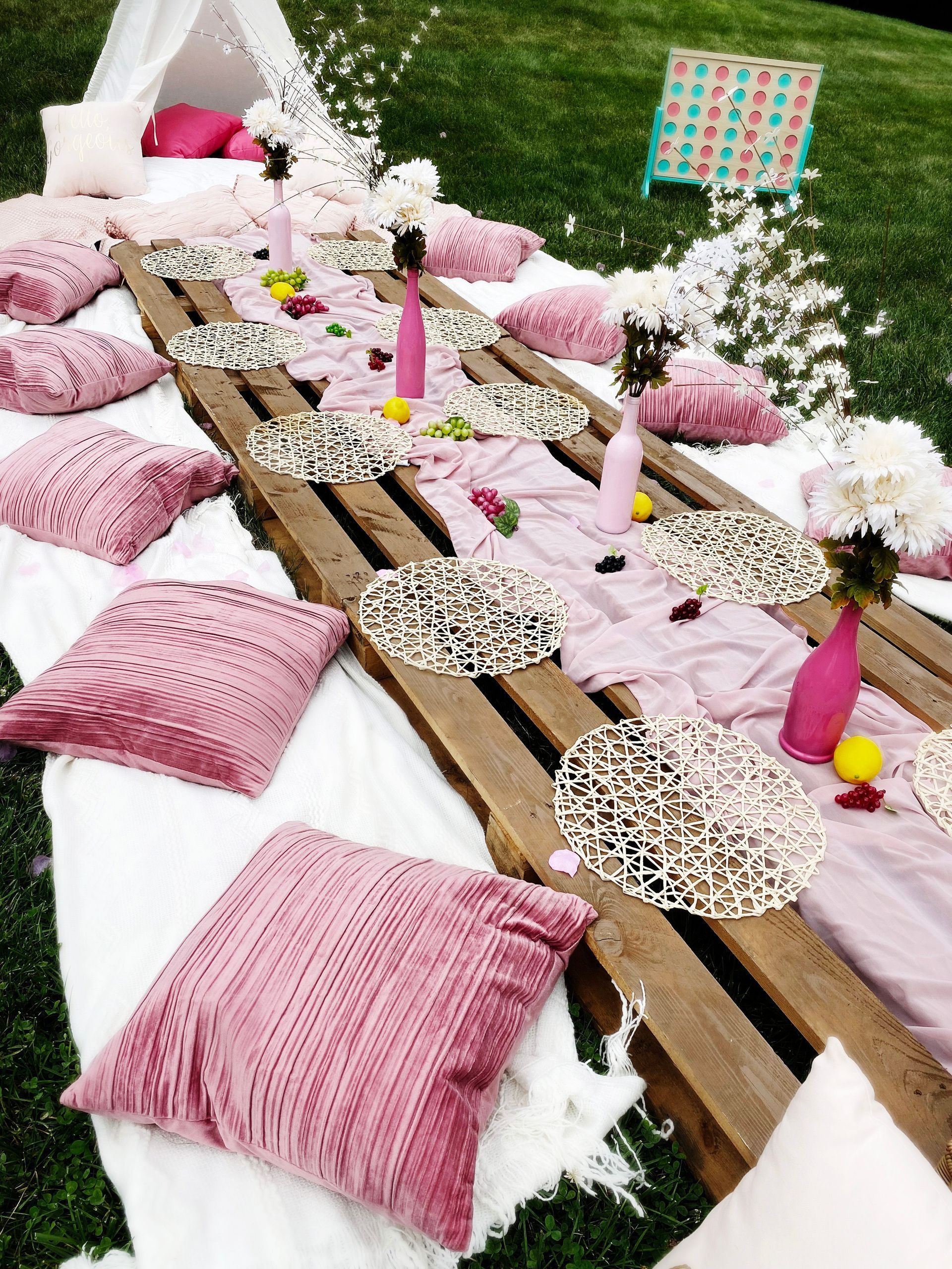 A long wooden table with pink pillows and flowers on it.