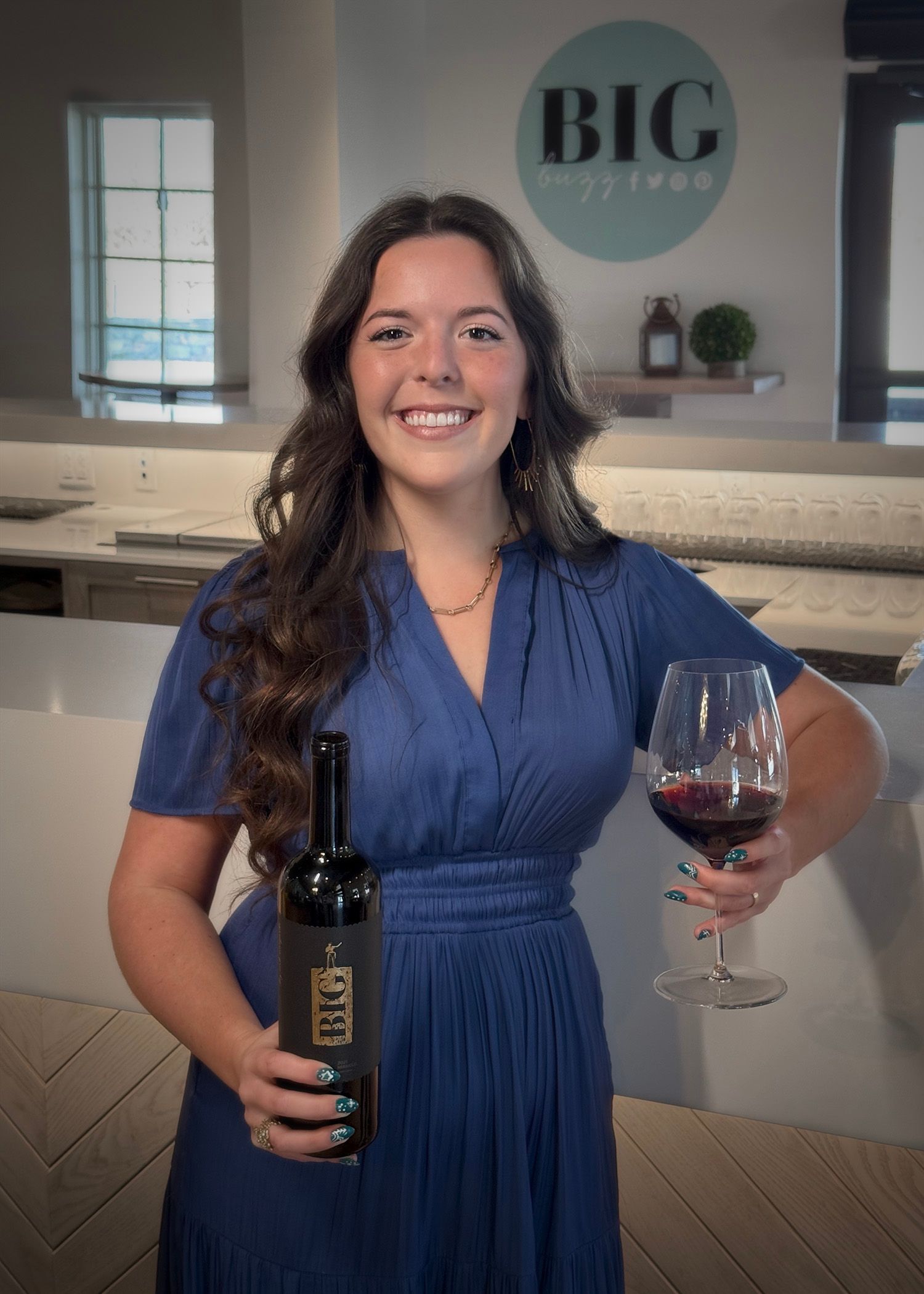 A woman in a blue dress is holding a bottle of wine and a glass of wine.