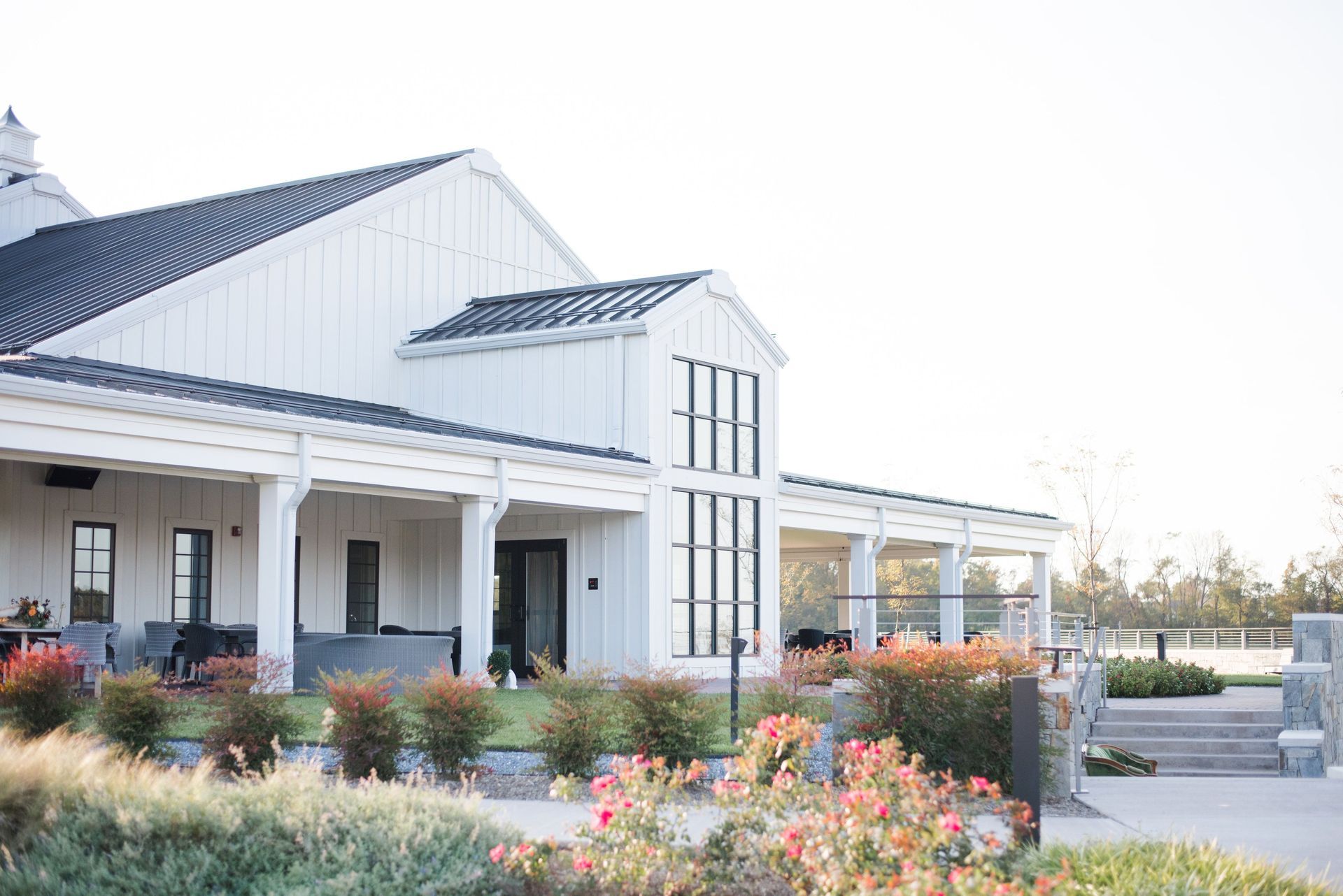 A large white barn with a porch and flowers in front of it.