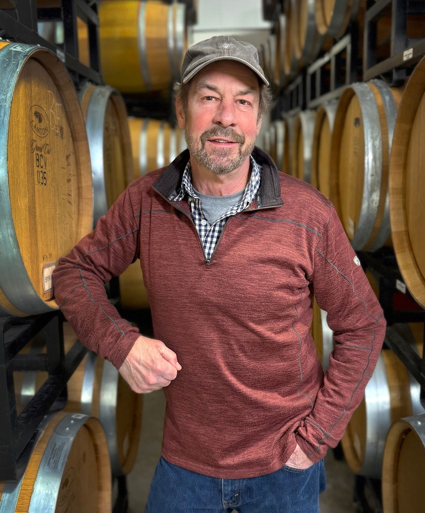 A man is standing in front of a row of wine barrels.