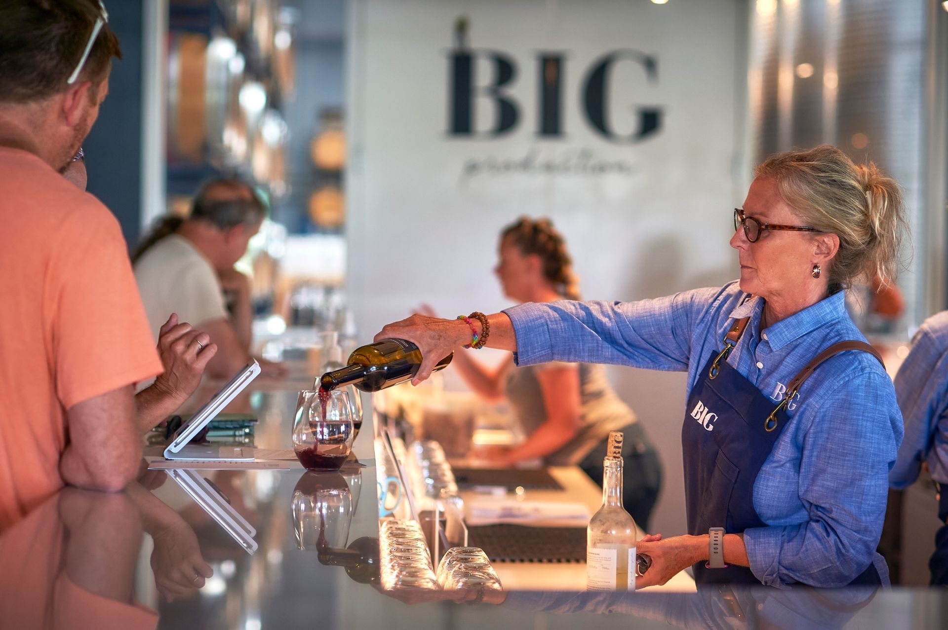 A woman is pouring wine into a glass at a bar.