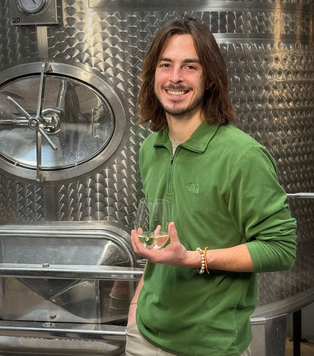 A man in a green shirt is holding a glass of wine