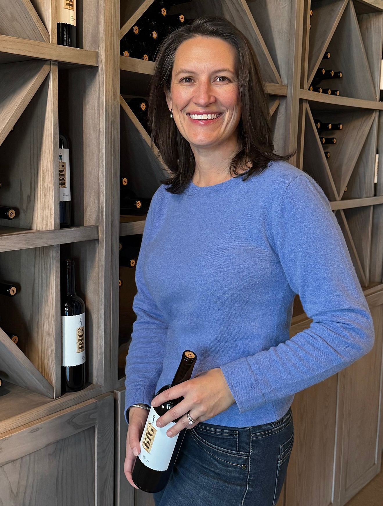 A woman in a blue sweater is holding a bottle of wine.