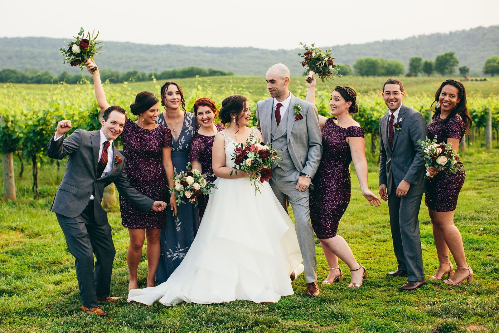 A bride and groom are posing for a picture with their wedding party in a vineyard.