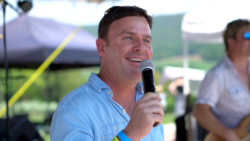 A man in a blue shirt is holding a microphone and smiling.
